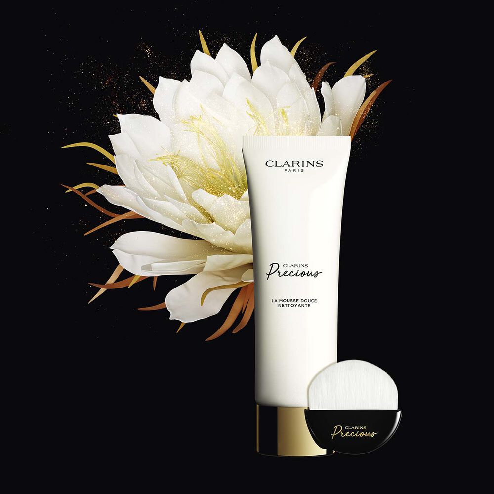 Packshot of the foaming cleanser tube and its dedicated face cleanser brush, displayed next to a shiny moonlight flower